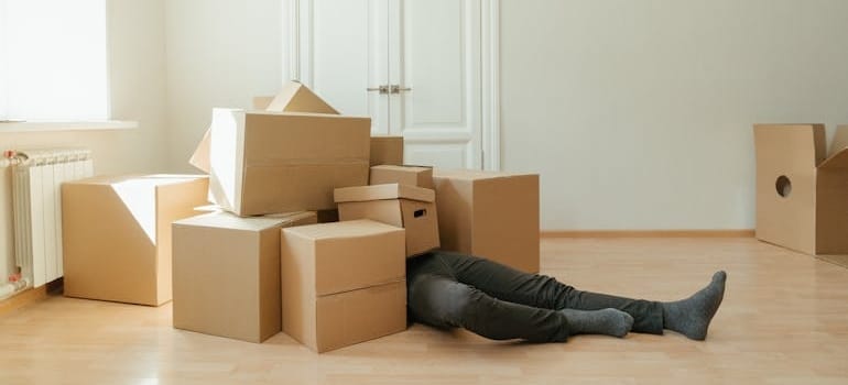 Man covered by cardboard boxes thinking about finding reliable storage for downsizing