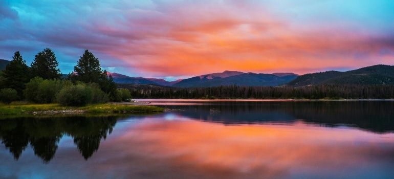 A tranquil lake in Colorado reflecting the vibrant hues of the sunset sky, showcasing the state's natural beauty.