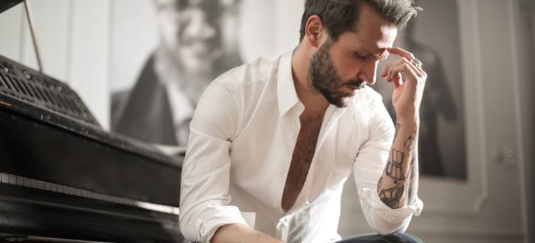 a man sitting next to a piano thinking about moving a rand piano