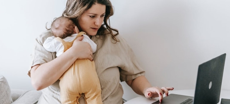 a woman holding a baby and browsing the net for relocation tips for single parents