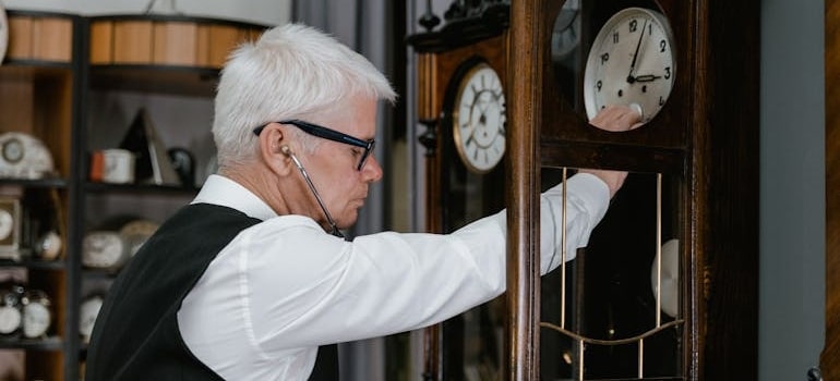 a man checking the pendulum of a clock before moving antique clocks to another place